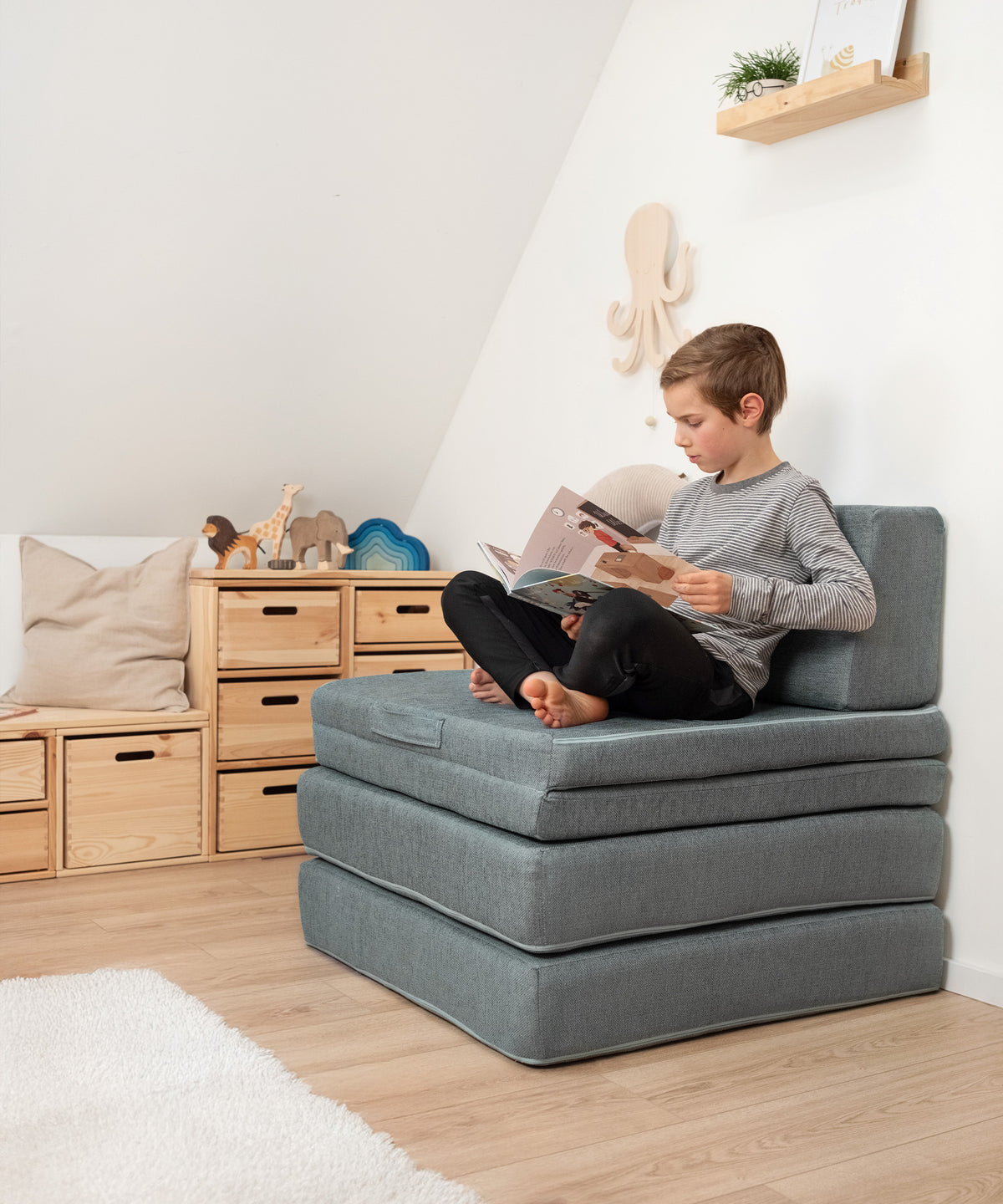 Kind liest auf dem zusammengeklappten Spielsofa.