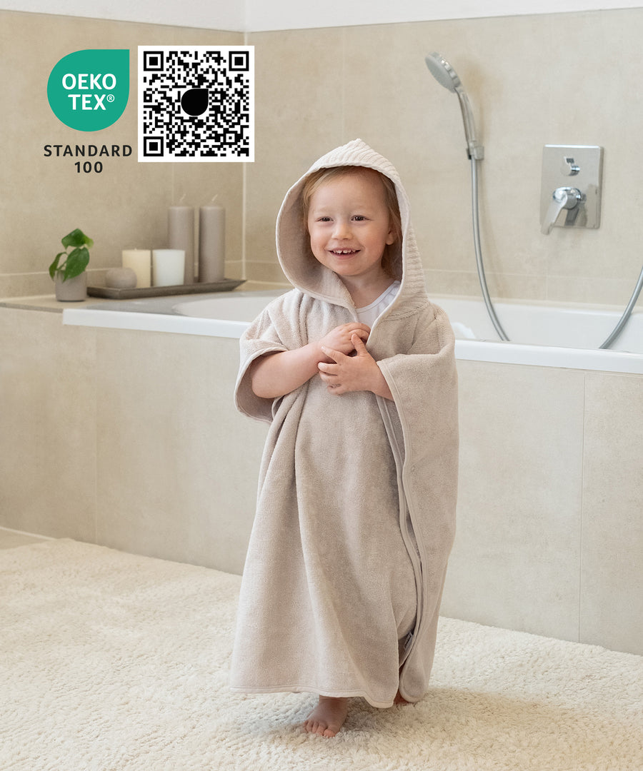 Kind trägt nach dem Baden einen weichen Badeponcho mit Kapuze.