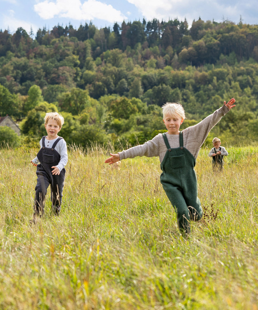 Kinder spielen im Feld und tragen die Walk-Latzhosen.