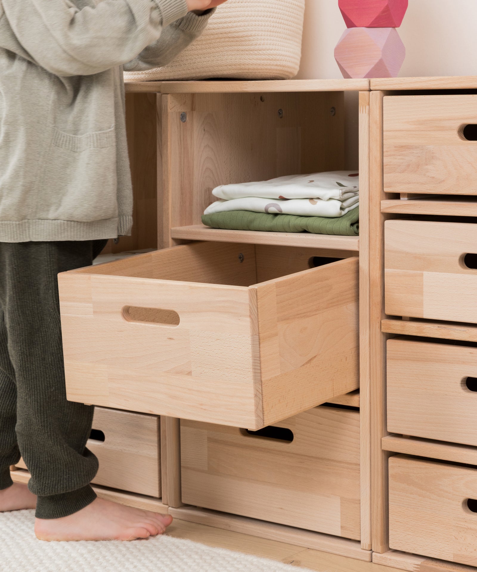 Kind räumt Kleidung selbstständig in das niedrige Regal ein.