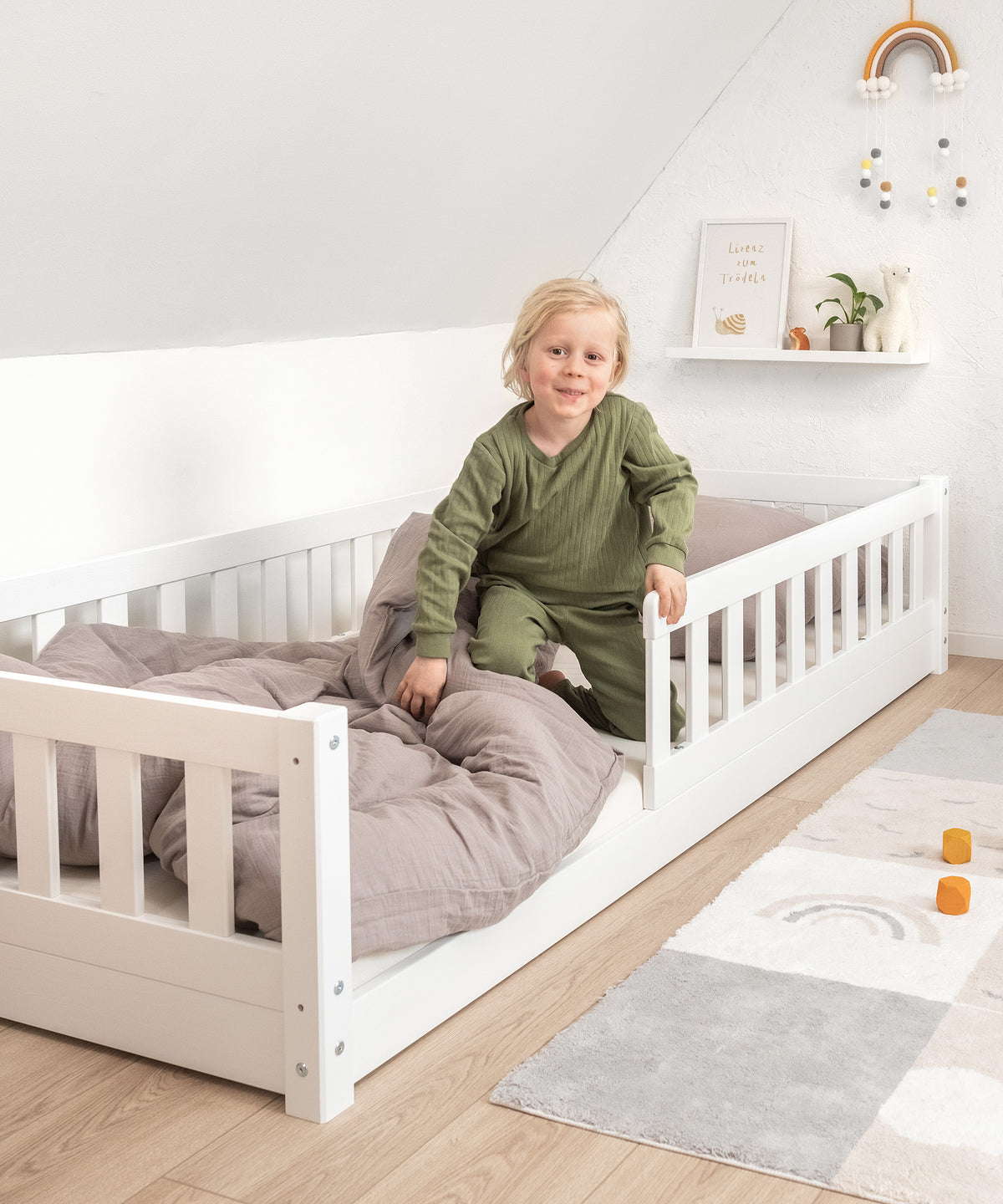 Kind steigt aus bodentiefem Bett aus Kiefer weiß lackiert.