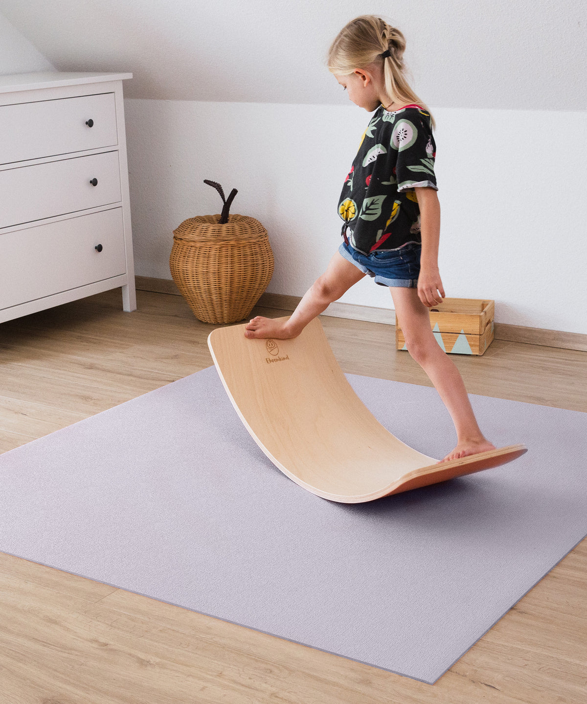 Kind balanciert mit BalanceBoard auf Krabbelmatte.