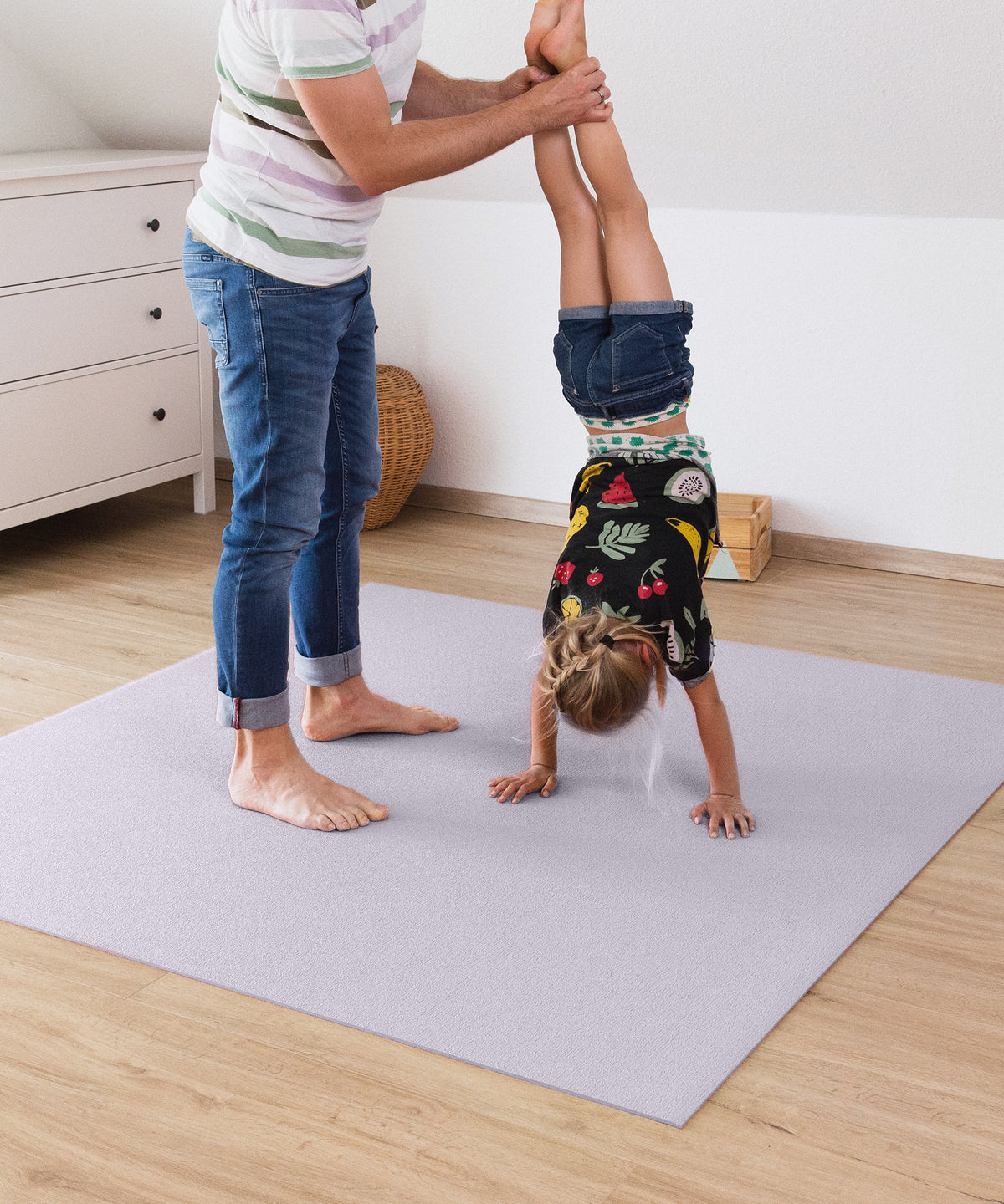 Kind macht Handstand auf Krabbelmatte und wird dabei an den Beinen gestützt.