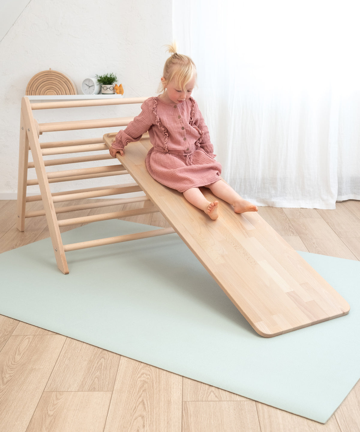 Kind rutscht von Kletterdreieck über Rutschbrett auf Krabbelmatte im Kinderzimmer.