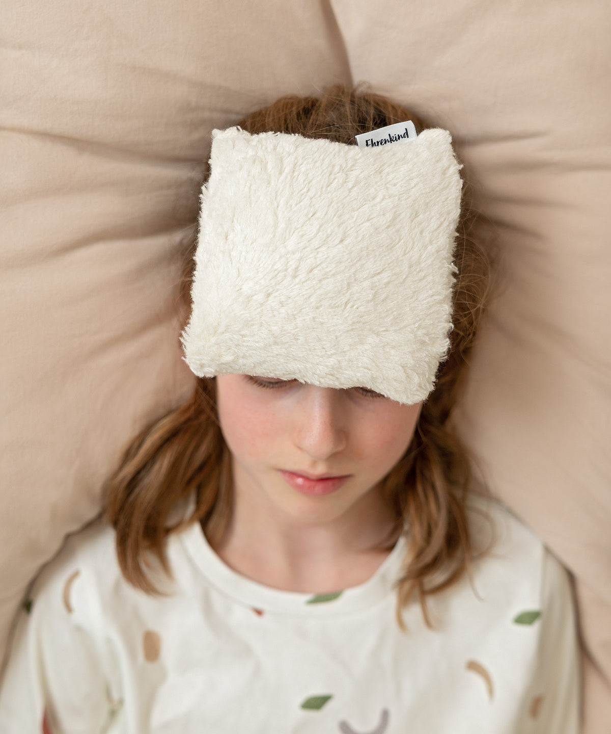 Kind hat das Kühlkissen auf der Stirn liegen.