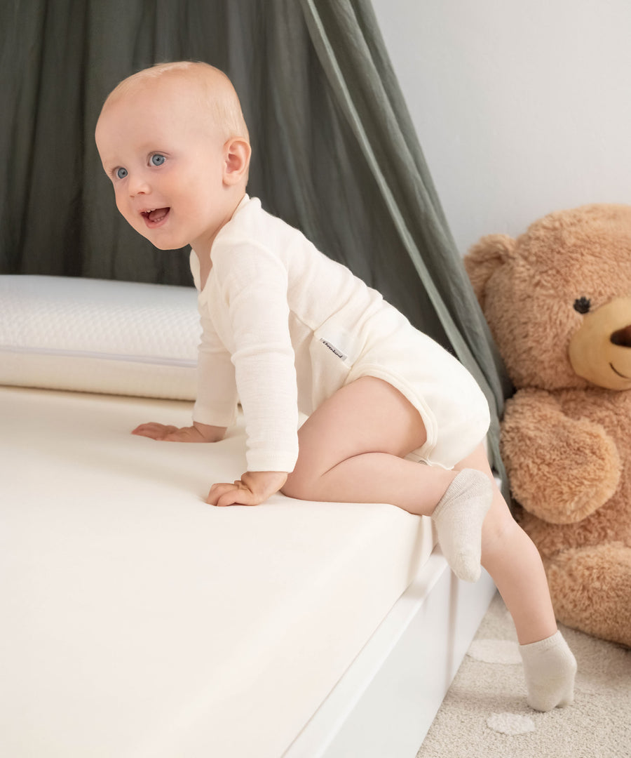 Temperaturausgleichend & sanft*Wie eine zweite Haut wärmt Merinowolle, wenn es kalt ist und kühlt, wenn es warm ist - der perfekte Begleiter zu jeder Jahreszeit.|Baby im Langarmbody klettert auf Bett.