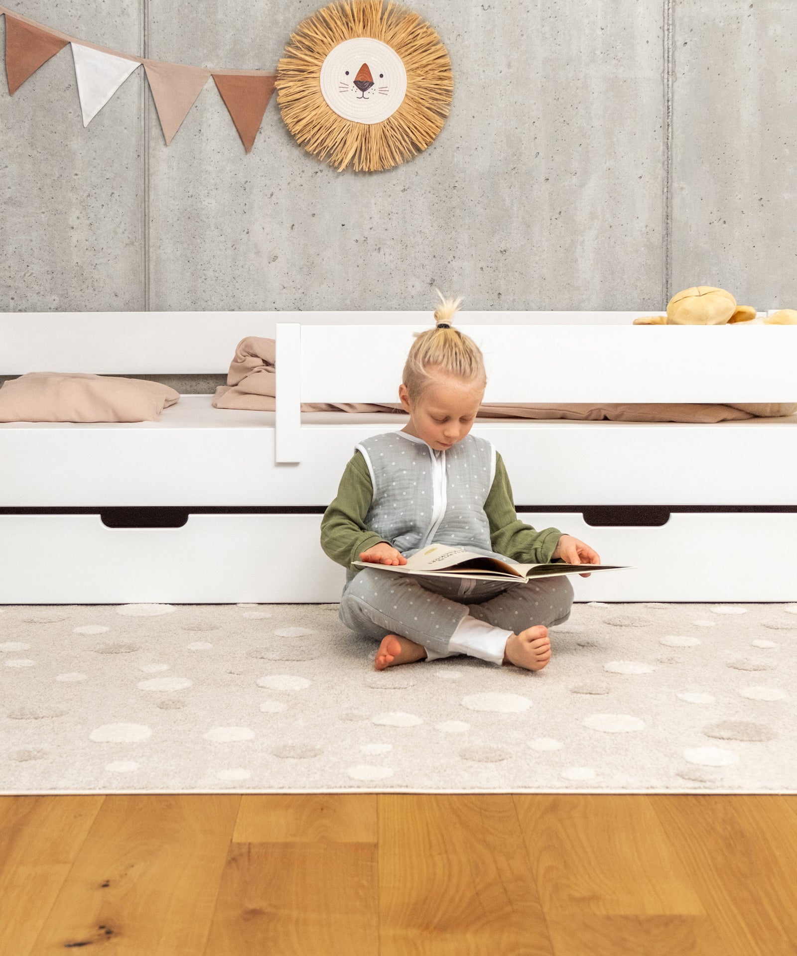 Lesendes Kind vor Kinderbett weiß mit Schubladen.