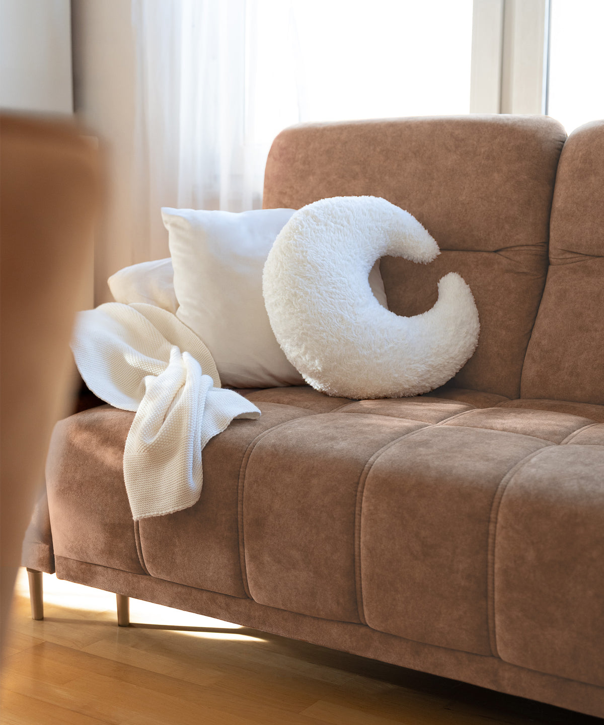 Mondförmiges Kuschelkissen aus Teddystoff auf Sofa.