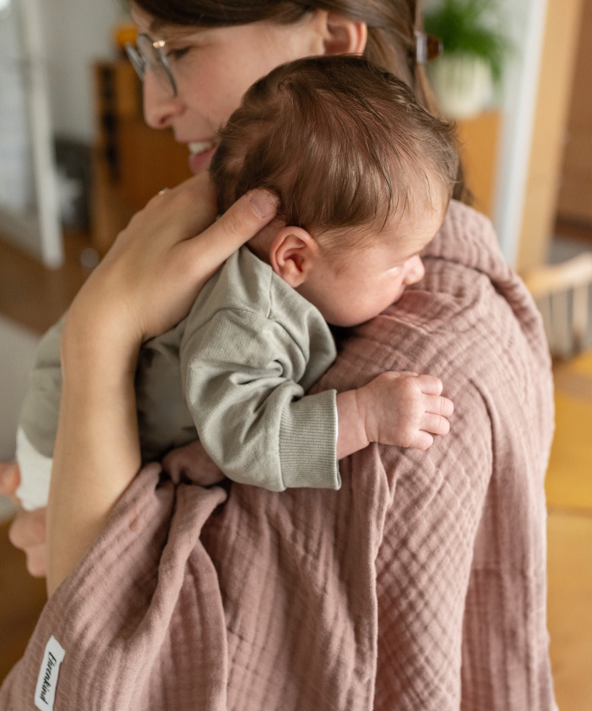 Mutter mit Baby und Wolltuch in Rose über der Schulter.