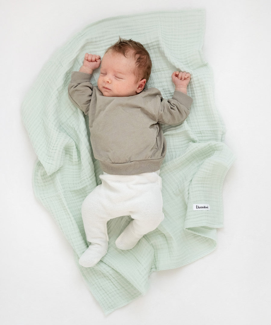 Baby liegt auf Mulltuch in Jade aus dem Mulltücher-Set Blau.