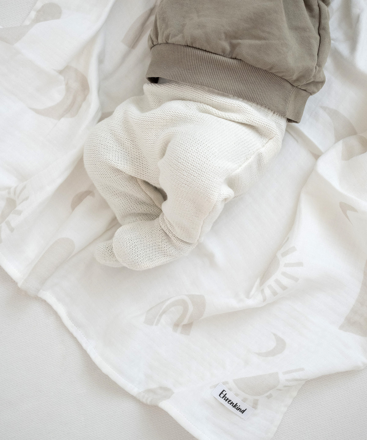 Baby liegt auf Mullwindel aus Farbvariante Beige mit Muster.