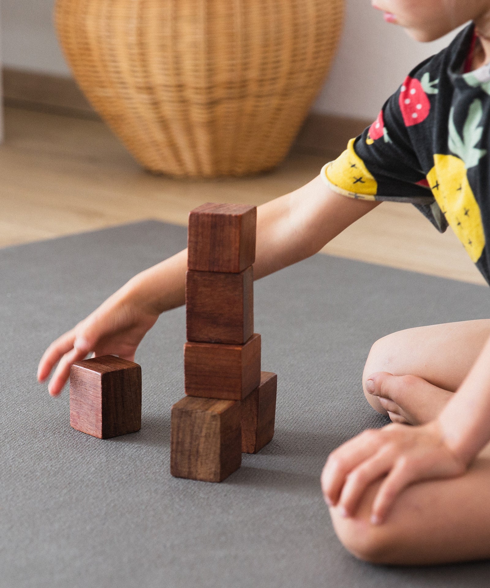 Kind spielt mit Holzklötzen auf Krabbelmatte.