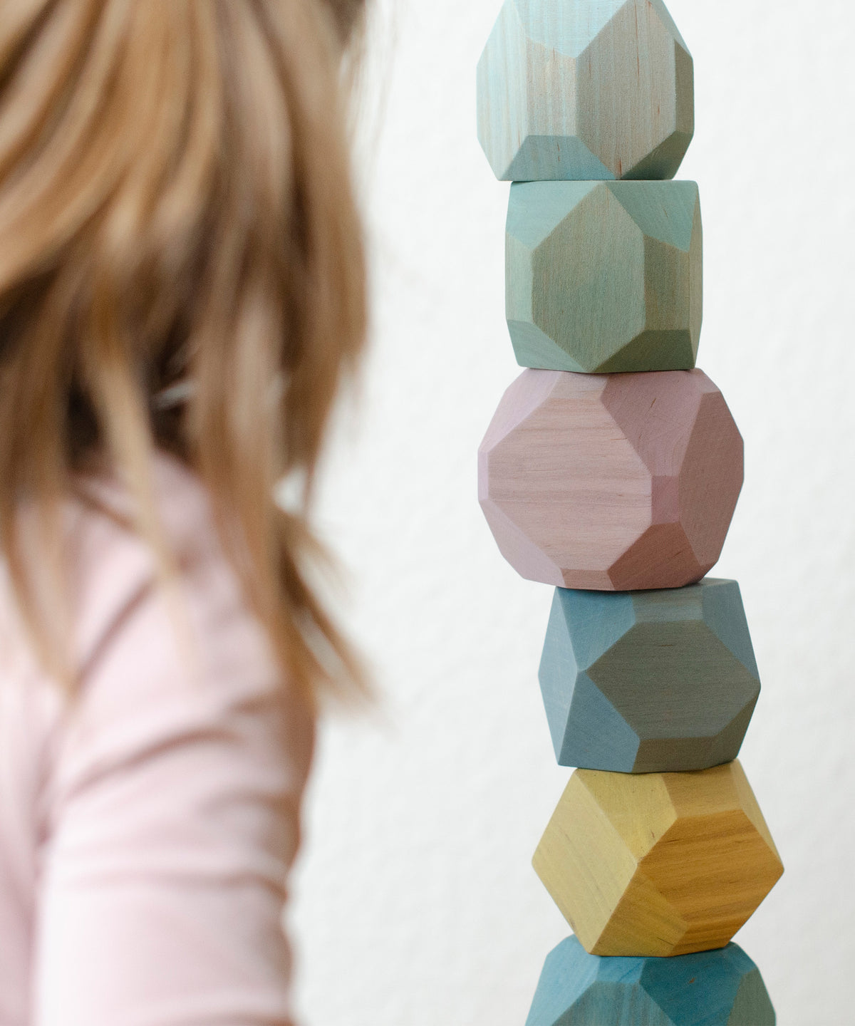 Mädchen stapelt Turm aus Balanciersteinen in bunten Pastellfarben.