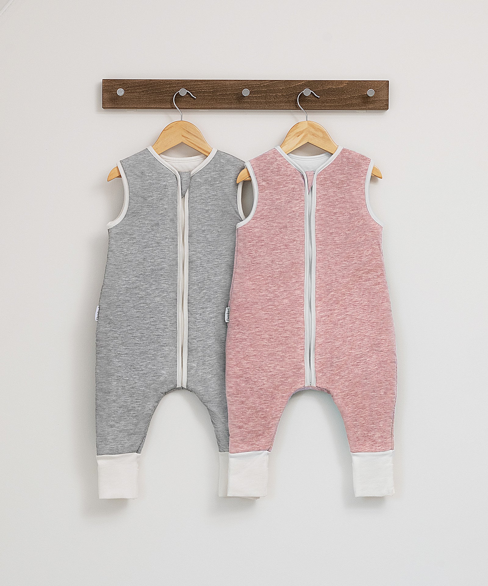 100% natürliche Materialien*Der Schlafsack aus Bio-Baumwolle mit reinster Schurwollfüllung bietet deinem Baby Geborgenheit und ein optimales Schlafklima.|Schlafsack in Rosé und Hellgrau auf dem Bügel.