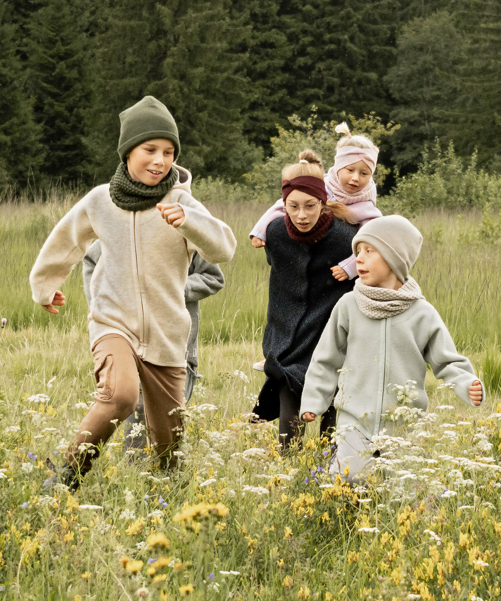 Fünf Kinder von klein bis groß rennen auf einem Feld.