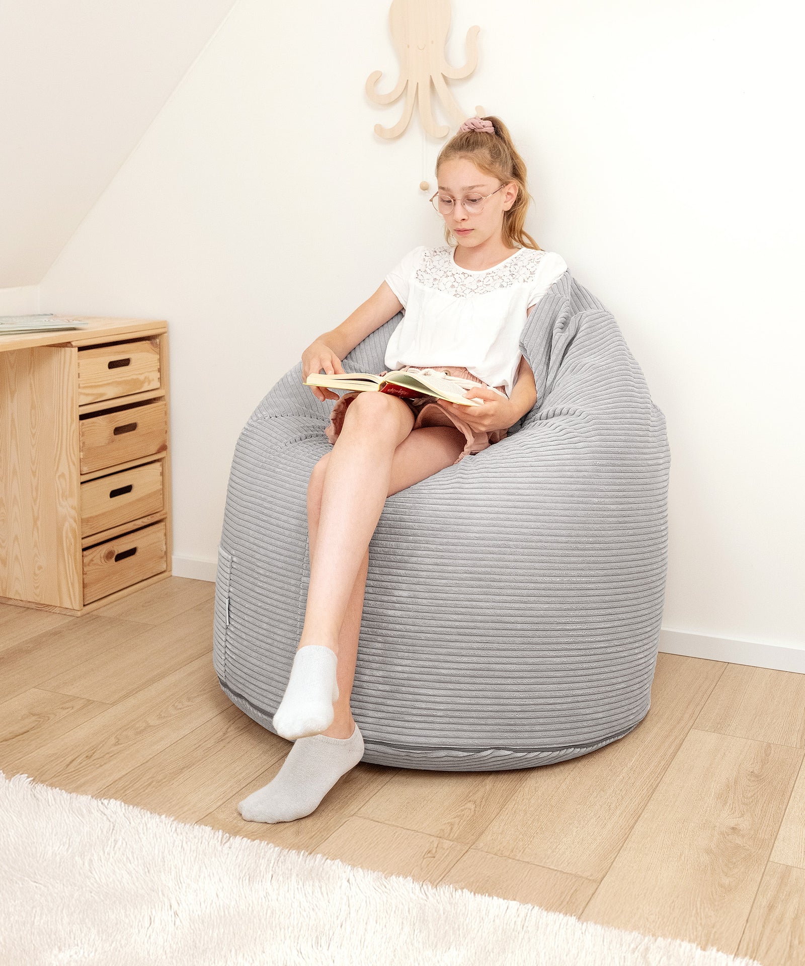 Entspannen leicht gemacht*Ideal zum Lesen, Spielen oder Relaxen - das flexible EPS-Granulat passt sich jeder Sitzposition ergonomisch an.|Mädchen sitzt im Kinder-Sitzsack in Grau und liest ein Buch.