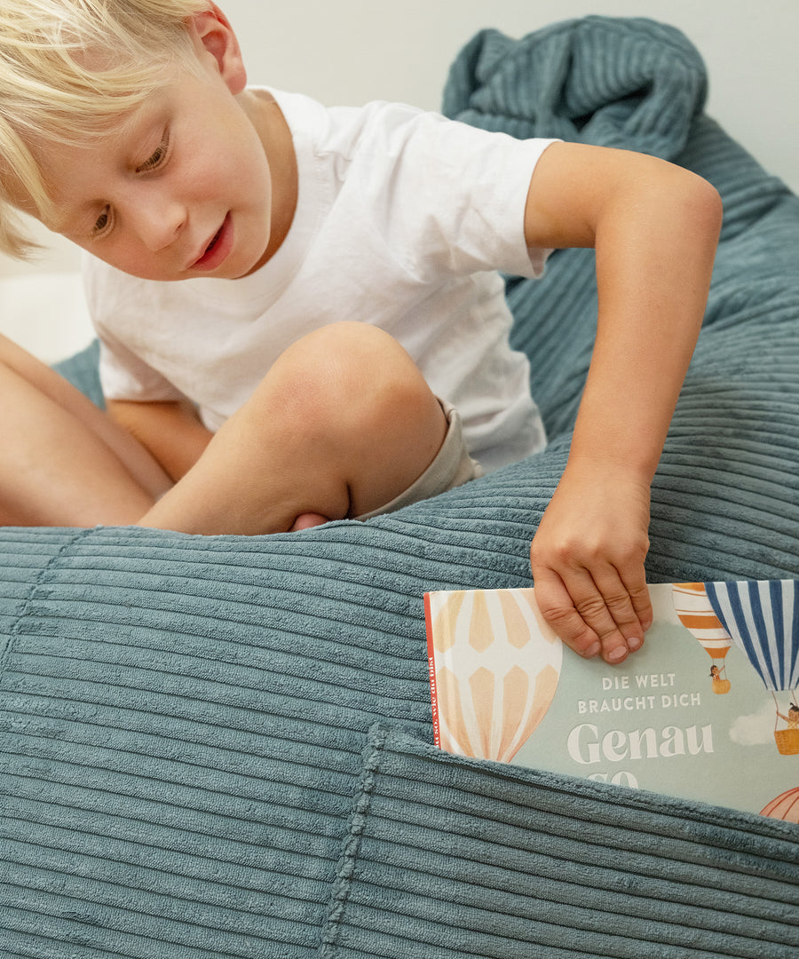 Kind zieht ein Buch aus der Seitentasche des Sitzsacks.