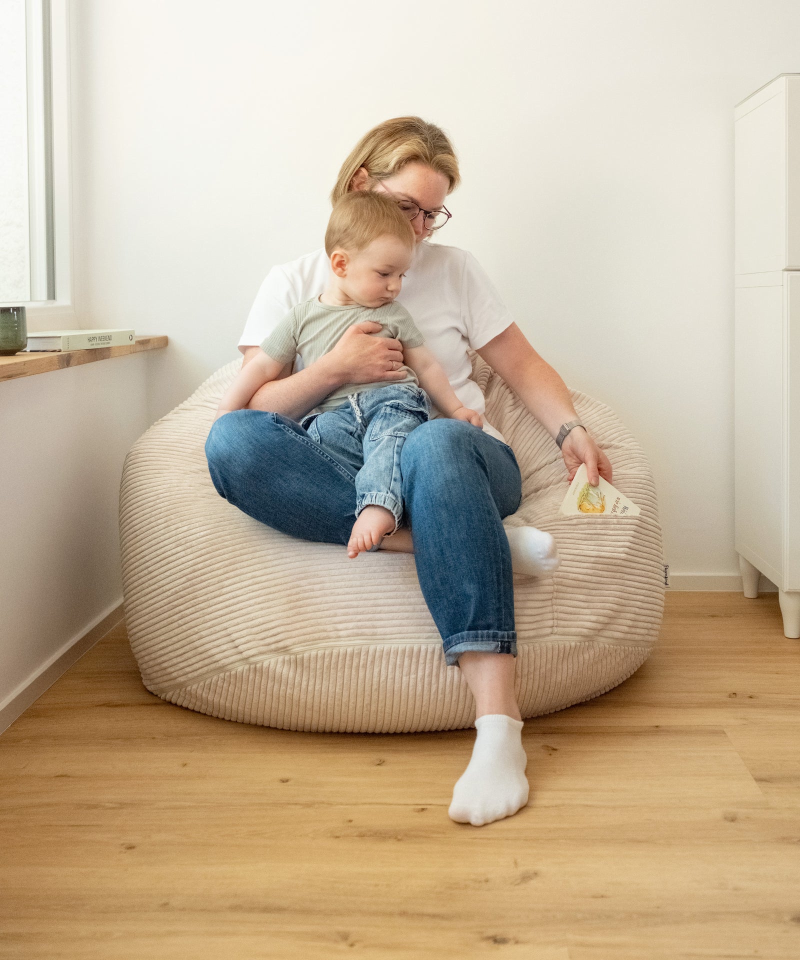 Mama sitzt mit Baby auf dem Sitzsack und zieht ein Buch aus der Seitentasche.
