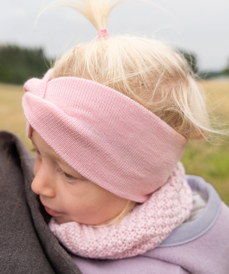 Ideal für Übergangszeiten*Temperaturregulierende Merinowolle wärmt im Herbst und fühlt sich im Frühling luftig an – für angenehmen Tragekomfort.| Mädchen trägt das rose Stirnband in der Natur.