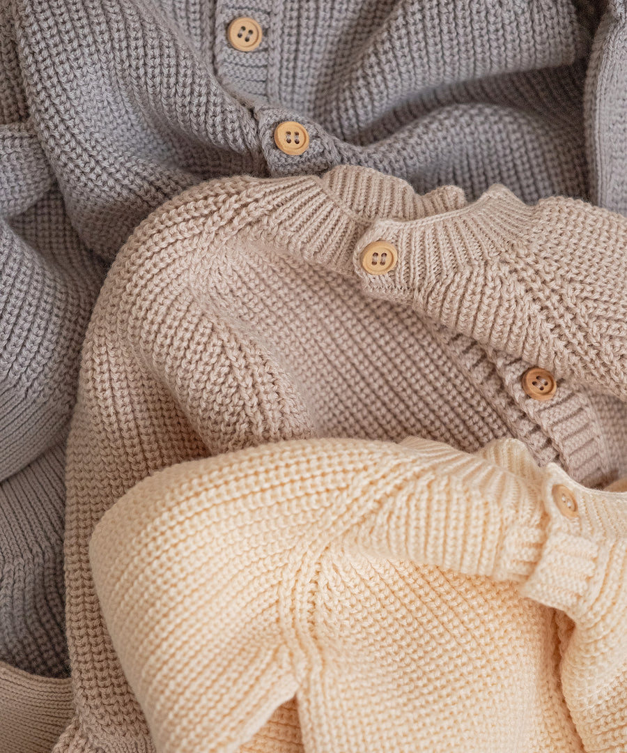 Detailaufnahme der Knopfleisten von drei Strickoveralls in verschiedenen Farben.