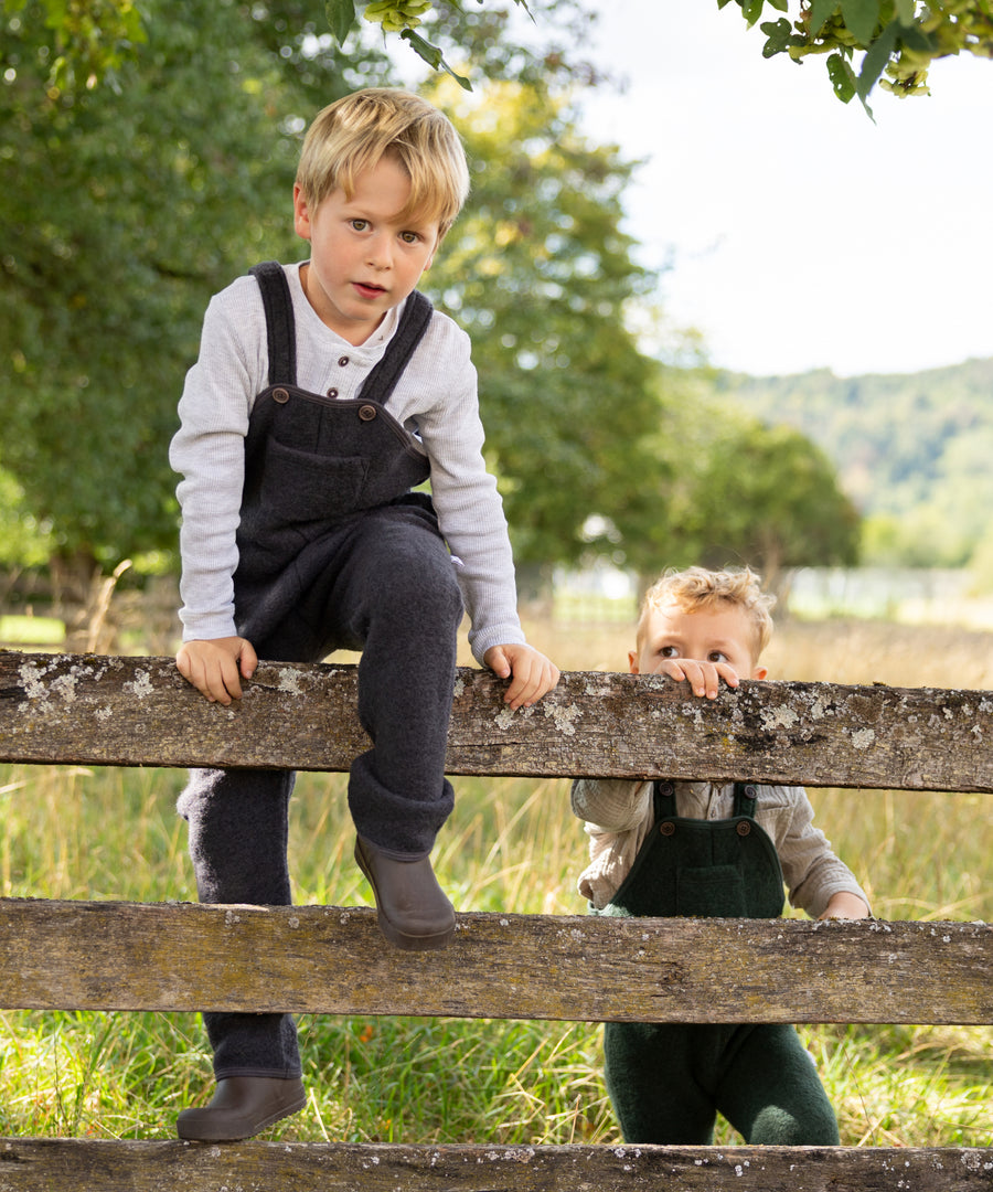 Kinder tragen die Walk-Latzhose in Anthrazit und Waldgrün.