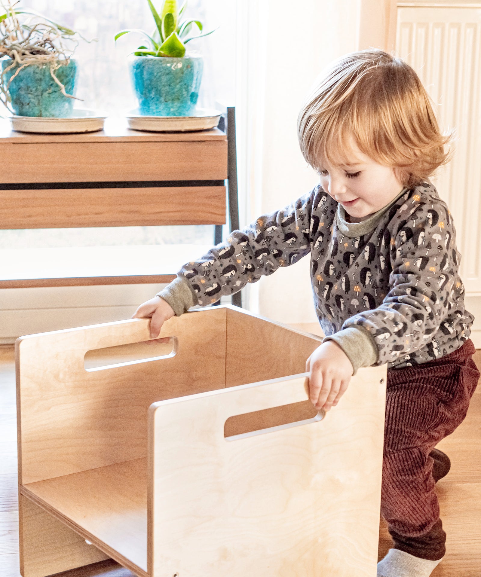 Kinderleicht & vielseitig*Aus Bank mach Tisch: Die praktischen Griffe ermöglichen es dir und deinem Kind, die Möbel ganz einfach zu greifen und zu wenden.| Kind steht an dem Wendehocker.