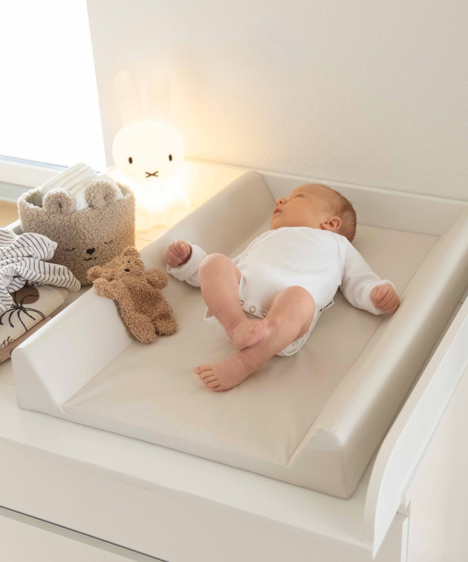 Baby liegt auf Wickelauflage Beige.