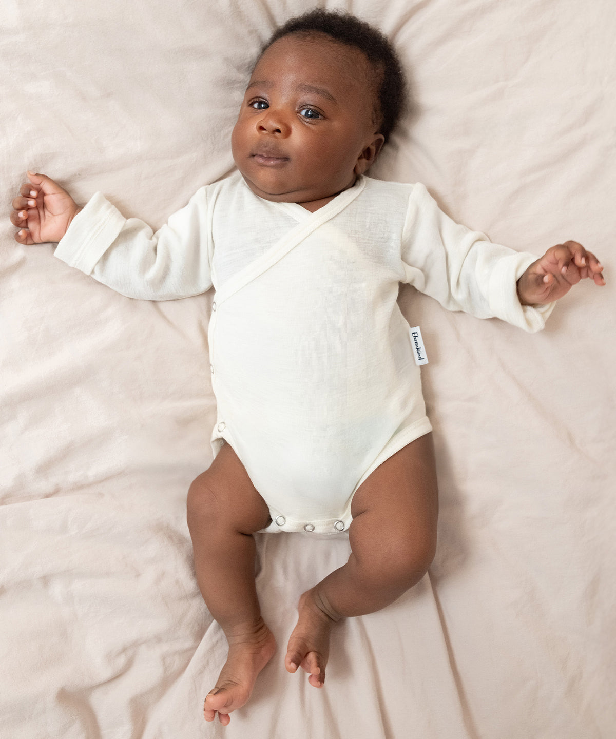 Klimaregulierende Eigenschaften*Merinowolle reguliert Feuchtigkeit, hält die Haut warm und trocken und kann so Hautausschlag bei Babys vorbeugen.|Baby liegt auf Bett.