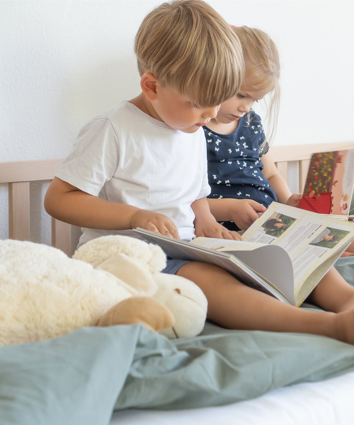 Zwei Kinder sitzen auf Hausbett Buche und schauen Bücher an.