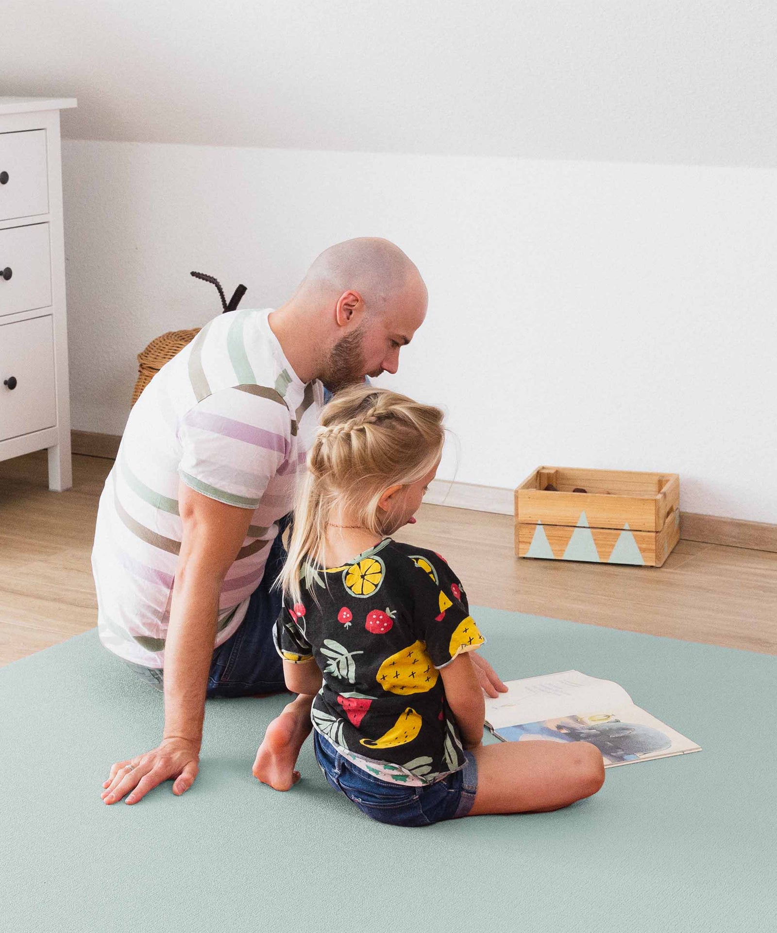 Mann und Kind lesen Buch auf Krabbelmatte.